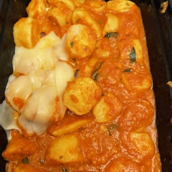 Olivadi - a close up of a dish of food - A black container holds gnocchi coated in a red tomato sauce with visible basil pieces. On one side, there is melted cheese, possibly mozzarella, covering some gnocchi. The dish appears freshly prepared and ready to serve, featuring classic Italian ingredients. - Italian Near Me - Norwood, Massachusetts