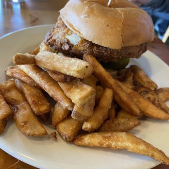 Upland Brewing - Bloomington - A fried chicken sandwich with a bun, fried chicken fillet, and toppings, served with French fries on a white plate. - American Near Me - Bloomington, Indiana