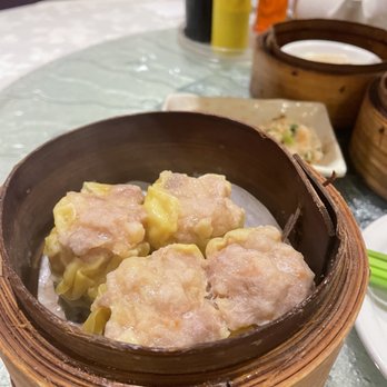 Dim Sum King - Shu mai - Four siu mai dumplings are placed in a bamboo steamer basket on a table at a dim sum restaurant, with condiments and other dishes visible in the background. - Dim Sum Near Me - Toronto, Ontario