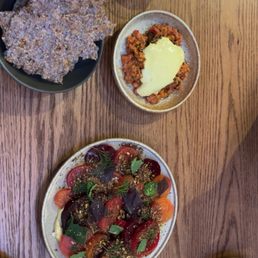 Beet Salad - The image shows a wooden table set with a beet salad, a meat dish topped with sauce, a crispy fried item, and several glasses of water and beverages.