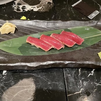 Sakaba - Seared tuna - Seared tuna slices are arranged on a green leaf on a black rectangular plate, accompanied by ginger and wasabi. - Sushi Bars Near Me - Avon, Colorado