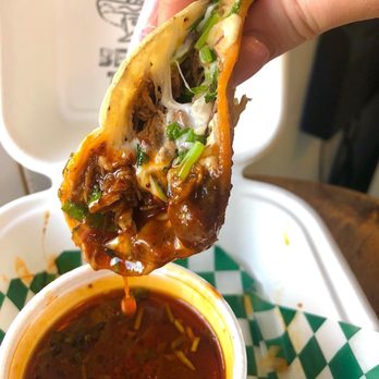 Benjo’s Tacos - a hand holding a taco over a bowl of sauce - Food Stands Near Me - Victoria, British Columbia Benjo’s Tacos - a hand holding a taco over a bowl of sauce - Food Stands Near Me - Victoria, British Columbia