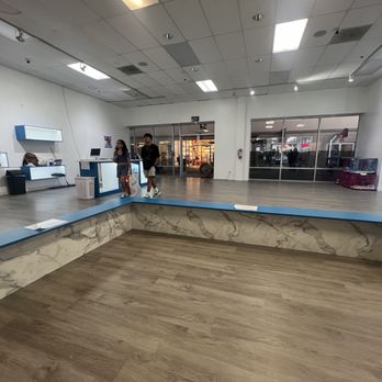 FureverPets - A vacant retail store interior with a marble and blue bench, wood flooring, and two people walking near the entrance, with store displays visible in the background. - Pet Stores Near Me - Round Rock, Texas
