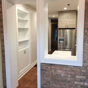 Demo Workers - A pass-through window in a brick wall connects the kitchen to an adjacent room, showing a stainless steel refrigerator and cabinetry. - General Contractors Near Me - Hubbard, Illinois