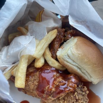 Uncle Remus - A hit - The image shows a takeout container filled with fried chicken topped with barbecue sauce, alongside French fries, a soft bread roll, and some napkins. The food appears freshly prepared and is arranged in a casual manner, typical of fast-food or takeout meals. - Chicken Wings Near Me - Chicago, Illinois