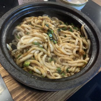Mr BoBo - Black pepper udon - Udon noodles with black pepper sauce served in a black stone bowl, garnished with chopped green onions, on a wooden tray. - Cantonese Near Me - Queens, New York