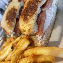 Turkey BLT - A close-up of a turkey BLT sandwich with toasted bread, bacon, turkey, and mayonnaise, served with French fries.