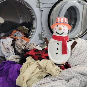 Laundry Palace - Out the washer - A snowman decoration with a hat, scarf, and buttons is positioned among laundry items in front of an open washing machine. - Laundry Services Near Me - Riverhead, New York