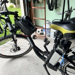 Both batteries - An electric bike with a child seat and a small bag is parked in a garage, with various tools and sports equipment visible in the background.