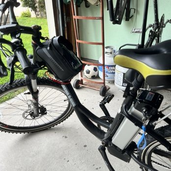 Pacific E-Bike - Both batteries - An electric bike with a child seat and a small bag is parked in a garage, with various tools and sports equipment visible in the background. - Bikes Near Me - Berkeley, California