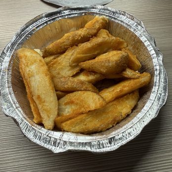 Anchor Bar - Potato Anchor Bar Wedges - A round aluminum foil container holds golden-brown potato wedges on a wooden table, with a partially visible lid in the background. - Chicken Wings Near Me - Buffalo, New York