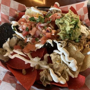 Whitlows - Nachos with chicken. Not exciting - A plate of nachos features tortilla chips topped with shredded chicken, guacamole, pico de gallo, sour cream, and shredded cheese. The dish is served on a checkered paper-lined basket, with some chips and toppings spilling over the edges. The presentation includes fresh ingredients and a variety of textures, typical of Mexican-style nachos. - Bars Near Me - Washington, DC, District of Columbia