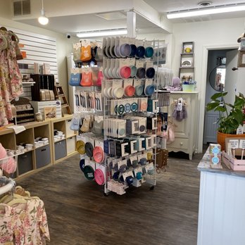 A Baby Naturally - A retail display rack in a baby store showcases an assortment of colorful bowls, plates, and kitchen accessories arranged on multiple tiers. The store interior features wooden flooring, shelves with baby clothing, toys, and gifts, and a white counter with a potted plant. The lighting is bright, and the store appears organized and inviting for shoppers interested in baby and nursery products. - Baby Gear & Furniture Near Me - Wheaton, Illinois