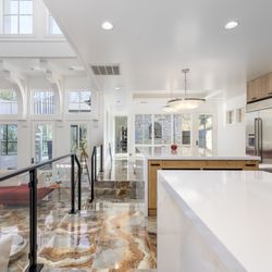 AGC Home Remodeling - Modern Austin kitchen with expansive counters, stainless appliances, porcelain floors, and glass railings to a bright open living area.
