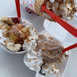 a hand holding a scoop of ice cream and a container of banana split a hand holding a scoop of ice cream and a container of banana split