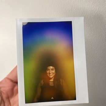 HausWitch - Aura photo - A woman with dark hair and a black outfit is smiling in an aura photograph with rainbow-colored light effects surrounding her. - Spiritual Shop Near Me - Salem, Massachusetts