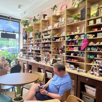 Miss Purl - Shop interior - A yarn store interior with wooden shelves filled with colorful yarns, plants, and craft supplies, with customers seated and browsing. - Knitting Supplies Near Me - Chicago, Illinois