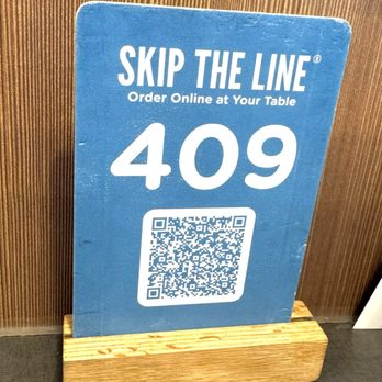 Culver's - The option to order online instead of waiting in line. - A blue sign with the text 'Skip the Line' and 'Order Online at Your Table,' displaying table number 409 and a QR code, placed on a wooden stand. - Ice Cream & Frozen Yogurt Near Me - Jacksonville, Florida