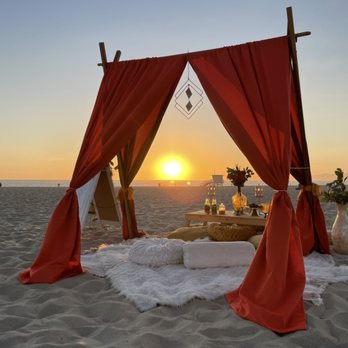 Picnic Heroes - Luxury picnic setup at the beach with a canopy, pillows, carpets, low picnic tables, flowers and decorations. - Party & Event Planning Near Me Picnic Heroes - Luxury picnic setup at the beach with a canopy, pillows, carpets, low picnic tables, flowers and decorations. - Party & Event Planning Near Me