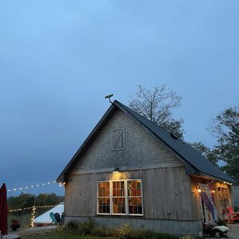Fluvial Brewing - A wooden building with large windows and outdoor seating, decorated with string lights, set against a twilight sky. - Breweries Near Me - Harrison, Maine