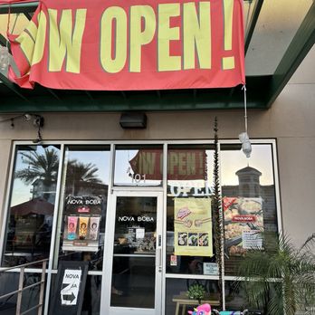 Nova Boba - Front of Nova Boba - The image shows the entrance of Nova Boba, a bubble tea shop, with a large red banner displaying "Now Open" hanging above the door. - Bubble Tea Near Me - Gilbert, Arizona