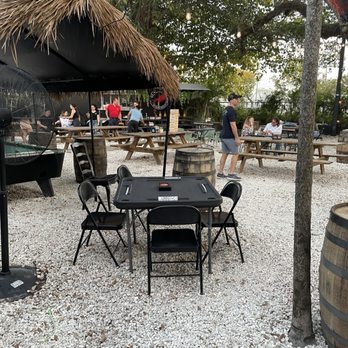Magic 13 Brewing - An outdoor patio at Magic 13 Brewing features picnic tables, barrels, string lights, and a thatched umbrella, with patrons dining and socializing. - Breweries Near Me - Miami, Florida