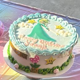 A round birthday cake decorated with a Super Mario theme, including stars, a mushroom, and a princess character on top.