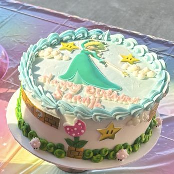 Smallcakes Cupcakery - A round birthday cake decorated with a Super Mario theme, including stars, a mushroom, and a princess character on top. - Cupcakes Near Me - Ripon, California