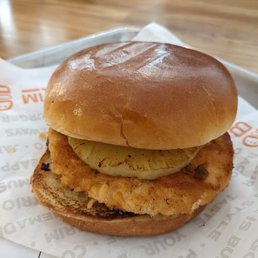 Salmon burger - A sandwich featuring a fried chicken patty, a slice of pineapple, and a soft bun, served on a tray with paper lining.