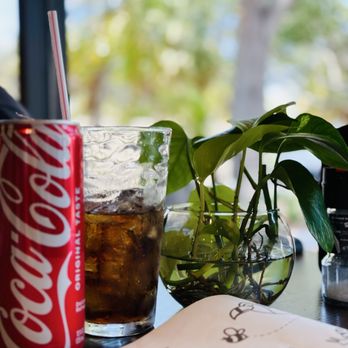 Arre - A Coca-Cola can, a glass of soda with ice, and a potted plant are placed on a table near a window with a blurred outdoor background. - Bakeries Near Me - Miami, Florida