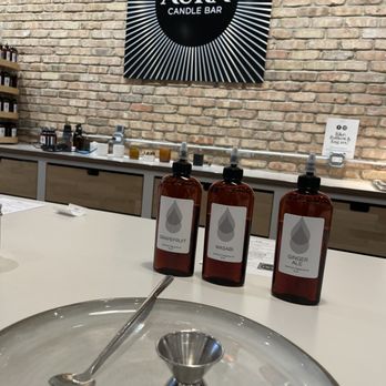 AURA Candle Bar - Three amber bottles labeled 'Grapefruit,' 'Wasabi,' and 'Ginger Ale' are arranged on a white counter inside Aura Candle Bar, Chicago. - Candle Stores Near Me - Chicago, Illinois