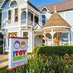 The Toy Chest - The Toy Chest storefront features a charming blue building, a welcoming porch, colorful signage, and lush gardens...