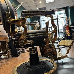 The B Room Barbershop - Ornate black leather barber chair with gold-plated frame and decorative studding in upscale barbershop.