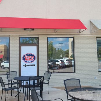 Jersey Mike's Subs - Jersey Mike's Subs storefront features large windows, a door with the logo, and outdoor seating with tables and chairs. - Fast Food Near Me - Bloomington, Indiana