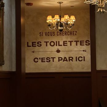 Petit Pomeroy - Inside upstairs - A wall sign in French with a chandelier overhead, directing customers to the toilets inside the establishment. - French Near Me - Chicago, Illinois