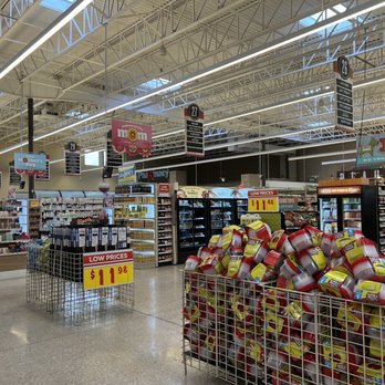 H-E-B - Overwhelming....everything is bigger in Texas - A grocery store aisle displays shelves with food and household items, promotional signs, and shopping carts filled with products. - Drugstores Near Me - Lakeway, Texas