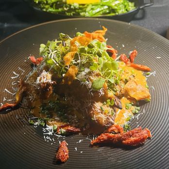 Flavorture - Airline Chicken - A dish featuring a main protein topped with microgreens, shredded cheese, and crispy garnishes, served on a black plate with a side of greens in the background. - Bars Near Me - Washington, DC, District of Columbia