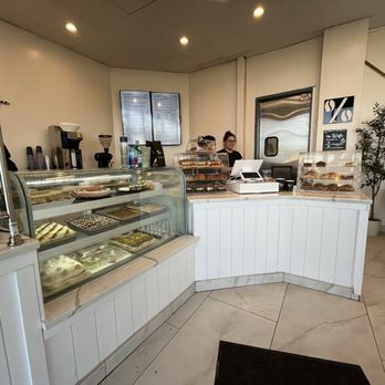 Percent Coffee - A coffee shop interior featuring display cases with pastries and baked goods, a counter with staff, and seating area in the background. - Coffee & Tea Near Me - Troy, Michigan