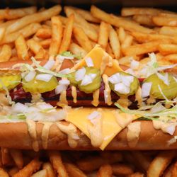 B'Shake Burger - Juicy beef hot dog on a soft bun with fresh lettuce, cheddar, pickles, onions, and signature B'Shake sauce, served with crispy fries.