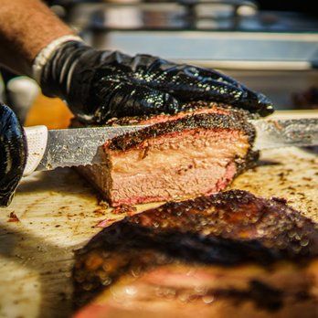 Oakhouse BBQ - a man cutting meat on a cutting board - Barbeque Near Me