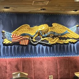 The American Spirit - Wall art depicts a golden eagle with outstretched wings, holding an American flag and a banner with Latin text, set against a dark background.