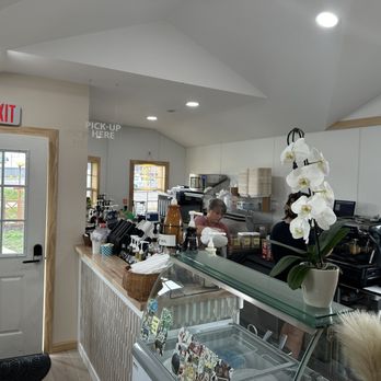 Trouvaille Coffee - Interior - A coffee shop interior featuring a counter with staff, coffee equipment, and a potted orchid plant, with a door and window in the background. - Breakfast & Brunch Near Me - New Glarus, Wisconsin
