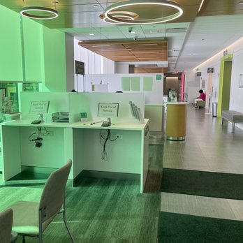 Rush South Loop - The image shows a hospital or medical center waiting area with white check-in kiosks marked as out of service, chairs, and a corridor with a person seated in the background. The ceiling has modern circular light fixtures, and the space is well-lit with natural and artificial light. The flooring includes green and gray carpet tiles, and the overall environment appears clean and organized. - Doctors Near Me - Chicago, Illinois