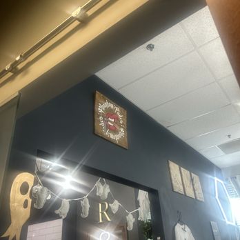 Phantom Fades - The photo captures an indoor area with dark-colored walls decorated with Halloween-themed items such as ghost and skull cutouts. There are framed artworks, including a sign with a mouth and the words 'Vandal's' and 'Vandal's' written around it. A white T-shirt with a graphic design hangs on a hook, and a small plant is visible in the background. The ceiling has a textured tile surface, and part of a person's arm is visible in the upper right corner. - Barbers Near Me - Gilbert, Arizona