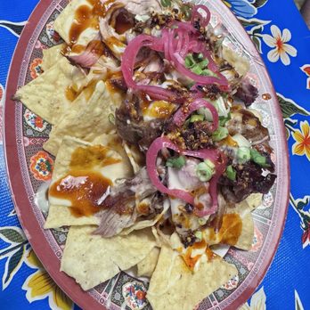Buck Tui BBQ - CHILI CRUNCH NACHOS Corn tortilla chips, cheese sauce, pulled pork, chili crunch, scallion, bog sauce, pickled red onion - Barbeque Near Me - Overland Park, Kansas