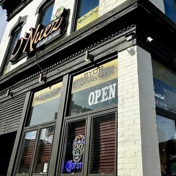 D' Nuez - BYOB it's Literally written on the Windows. - A restaurant storefront with large windows displaying an 'OPEN' sign and a neon skull logo, with the name 'El Nopal' above. - Latin American Near Me - Chicago, Illinois
