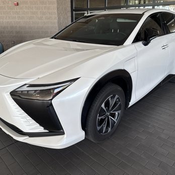 Arrowhead Lexus - Lexus RZ - A white Lexus RZ electric SUV is displayed indoors at Arrowhead Lexus dealership in Peoria, AZ, with other vehicles visible nearby. - Car Dealers Near Me - Peoria, Arizona