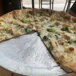 Chicken 14" Barbecue Chicken Pizza - A chicken and broccoli pizza on a metal tray, with a restaurant interior and large windows in the background.