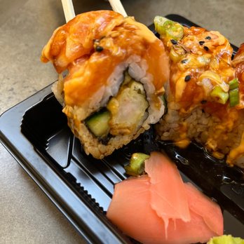 Sushi-Q - Spicy salmon dragon - A sushi roll with salmon, cucumber, and sauce is held with chopsticks over a black tray, with pickled ginger and wasabi on the side. - Sushi Bars Near Me - Buffalo, New York