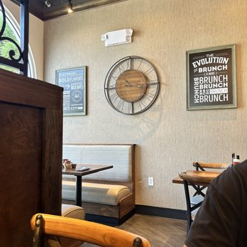Another Broken Egg Cafe - Inside - A restaurant interior features a beige wall with wall art, a clock, and a window with decorative ironwork. - Breakfast & Brunch Near Me - Austin, Texas